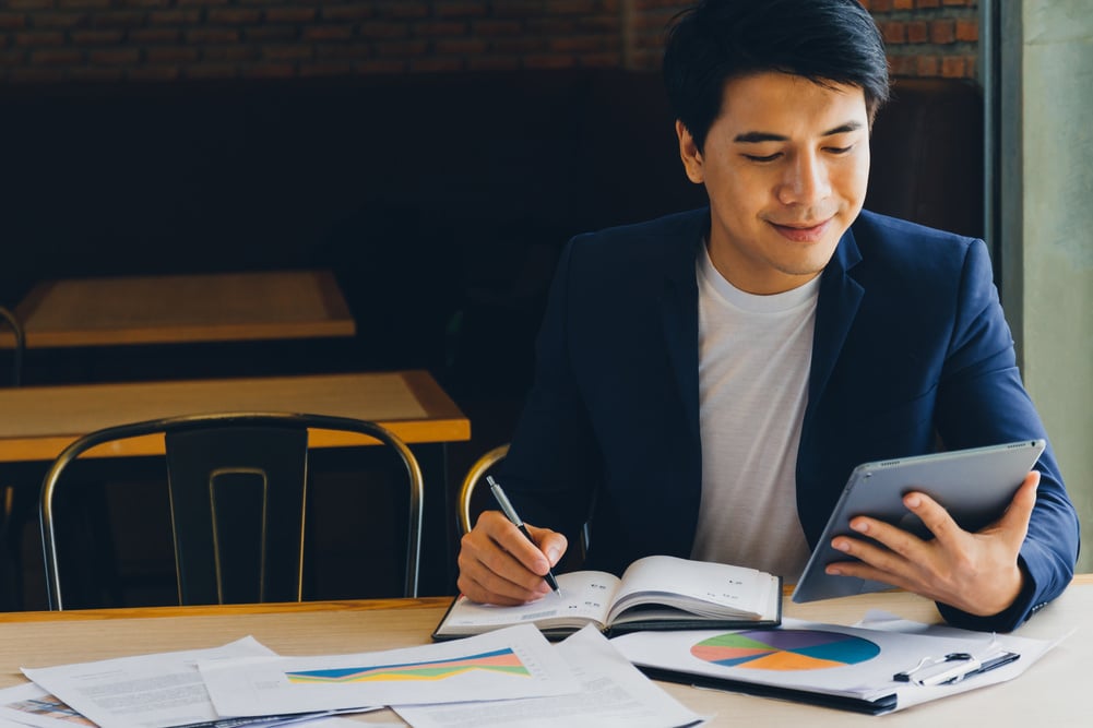 Businessman using tablet and analyzing investment charts in a cafe.